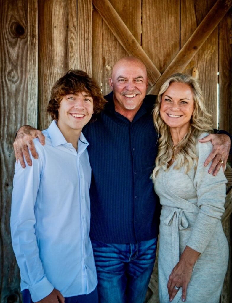 Dr. Robert Tieperman with one arm around his teenage son, and the other around his wife. All wear radiant smiles.